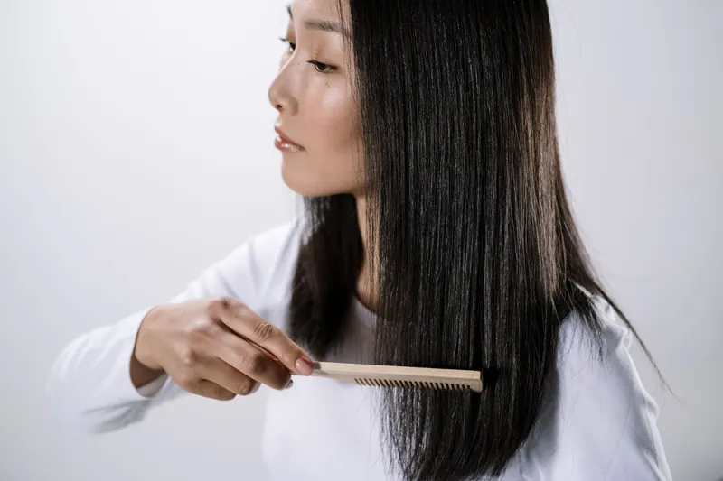 Studio portrait of an Asian woman combing her straight black hair indoors with a white background