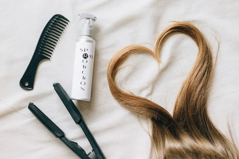 Flat lay of hair styling tools on a bedsheet with heart-shaped hair strand