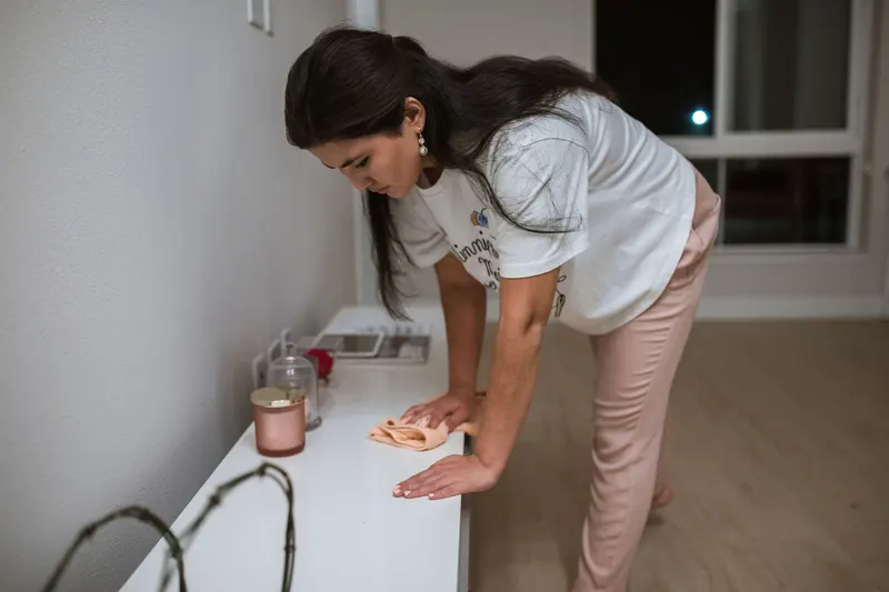 Woman wiping a white table with cloth indoors at night, engaging in household cleaning chores