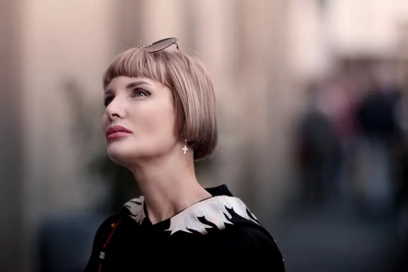 Stylish portrait of a woman with blonde bob haircut and sunglasses, looking up with a blurred urban background