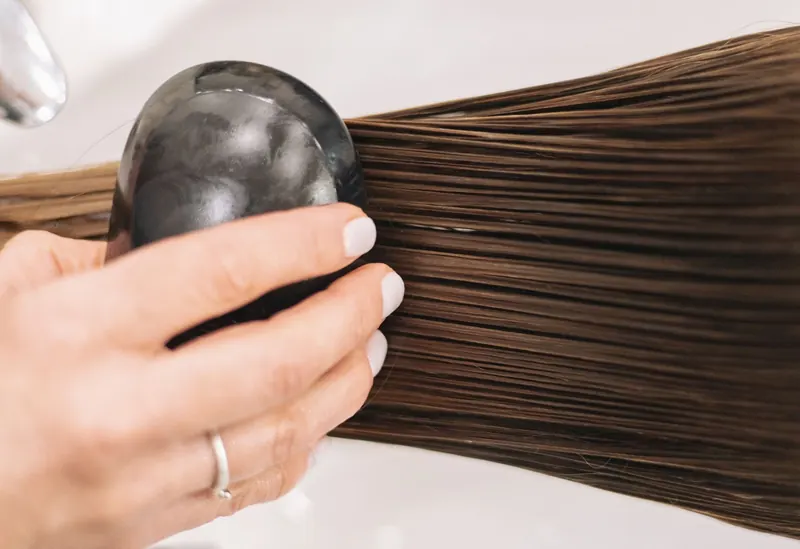 Close-up of a woman brushing long brown hair with a black brush, highlighting hair care and grooming