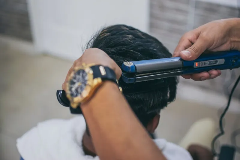 Close-up of a hairdresser styling a client's hair using a straightener in a barbershop