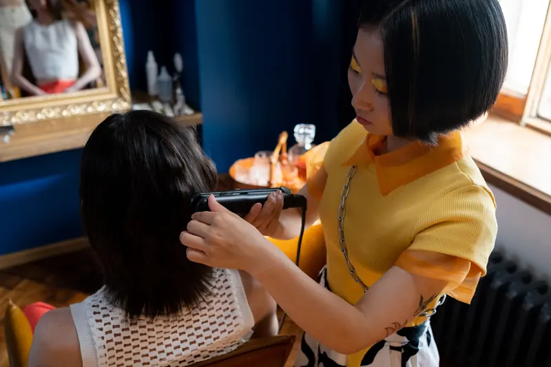 A hairdresser styles a client's hair with a straightener in a modern salon setting